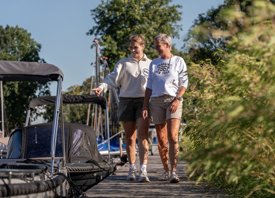 Frauen gehen am Steg entlang, vorbei an den Schaluppen von Maran Yachtcharter